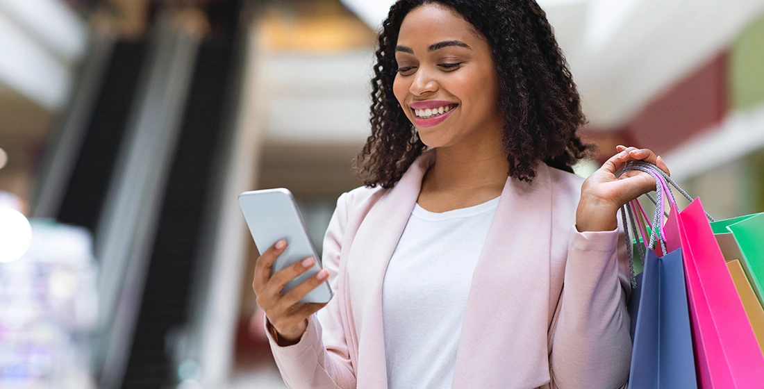 woman holding shopping bags while using her smartphone